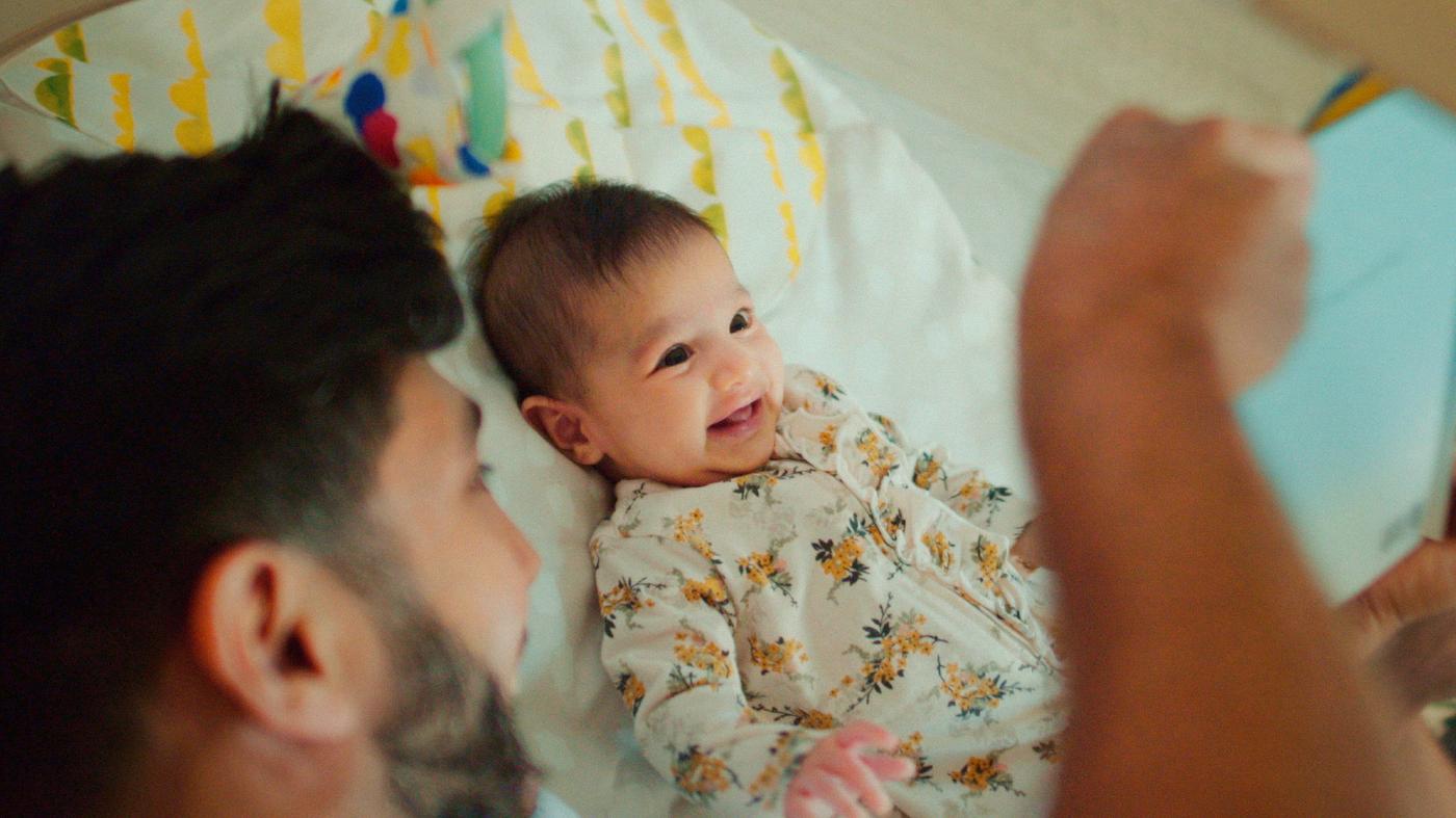A man with a beard entertains a smiling baby on a bed.