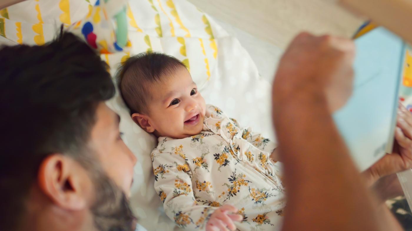 A man with a beard entertains a smiling baby on a bed.