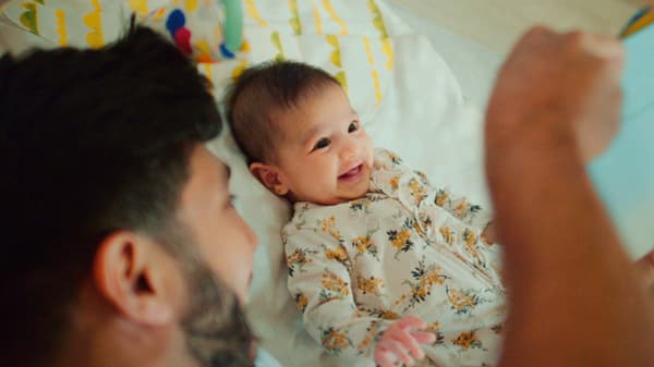 A man with a beard entertains a smiling baby on a bed.