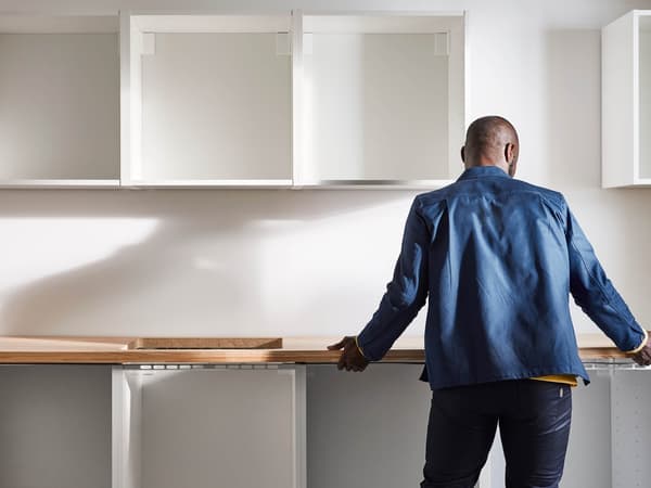 A man with his back turned in a partially finished kitchen and holds a kitchen countertop.