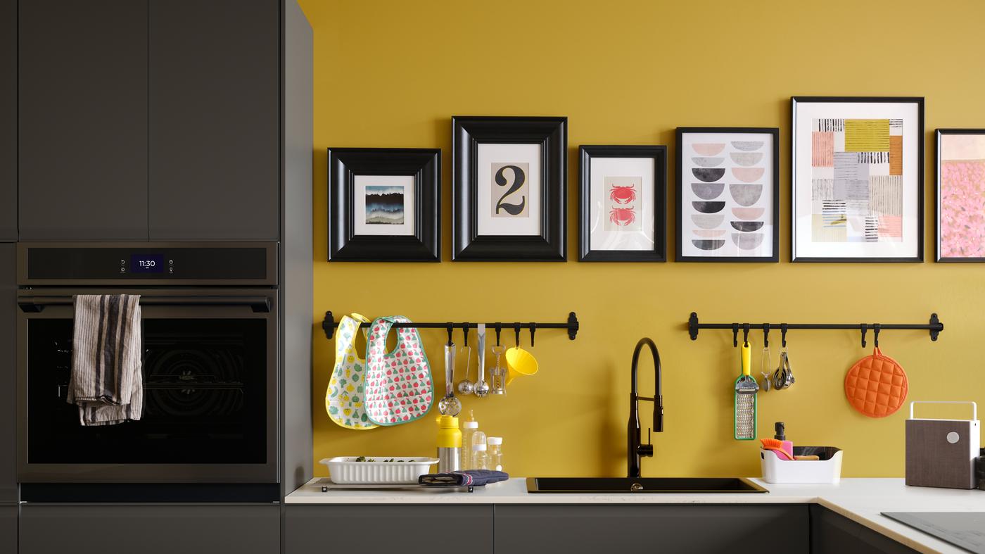 A matte anthracite kitchen with a white marble effect worktop, plus black rails and pictures in black frames on a yellow wall.