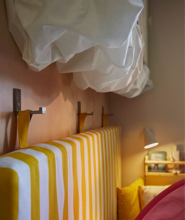 A mattress hung from hooks on the wall beside a bed. White fabric attached under wall cupboards for cloud-like shapes.