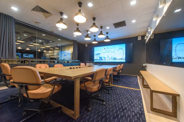 A meeting area with a long wooden table and swivel chairs placed on top of a dark blue carpet. 