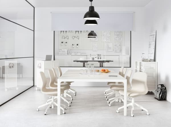 A meeting room with a glass wall containing a large white table. A row of black SKURUP pendant lamps hang from the ceiling.