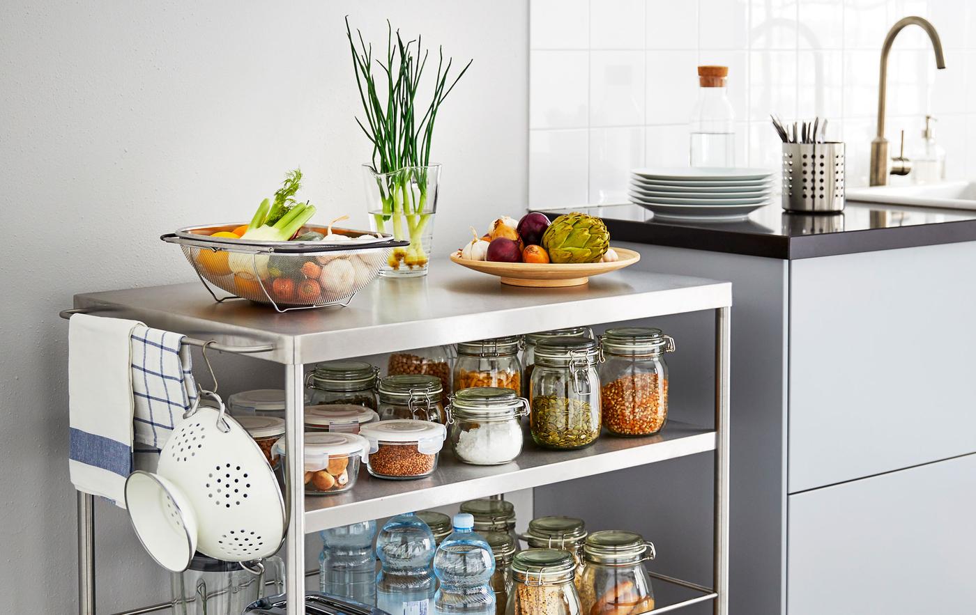 A metal kitchen island on wheels stocked with jarred ingredients sits next to a kitchen counter.