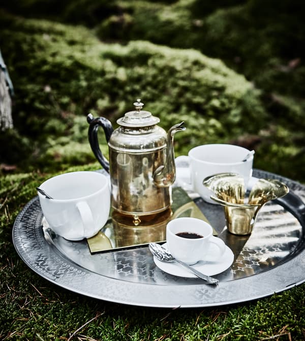 A metal tray with cups of tea, coffee and a kettle resting on the ground in a forest wedding lounge