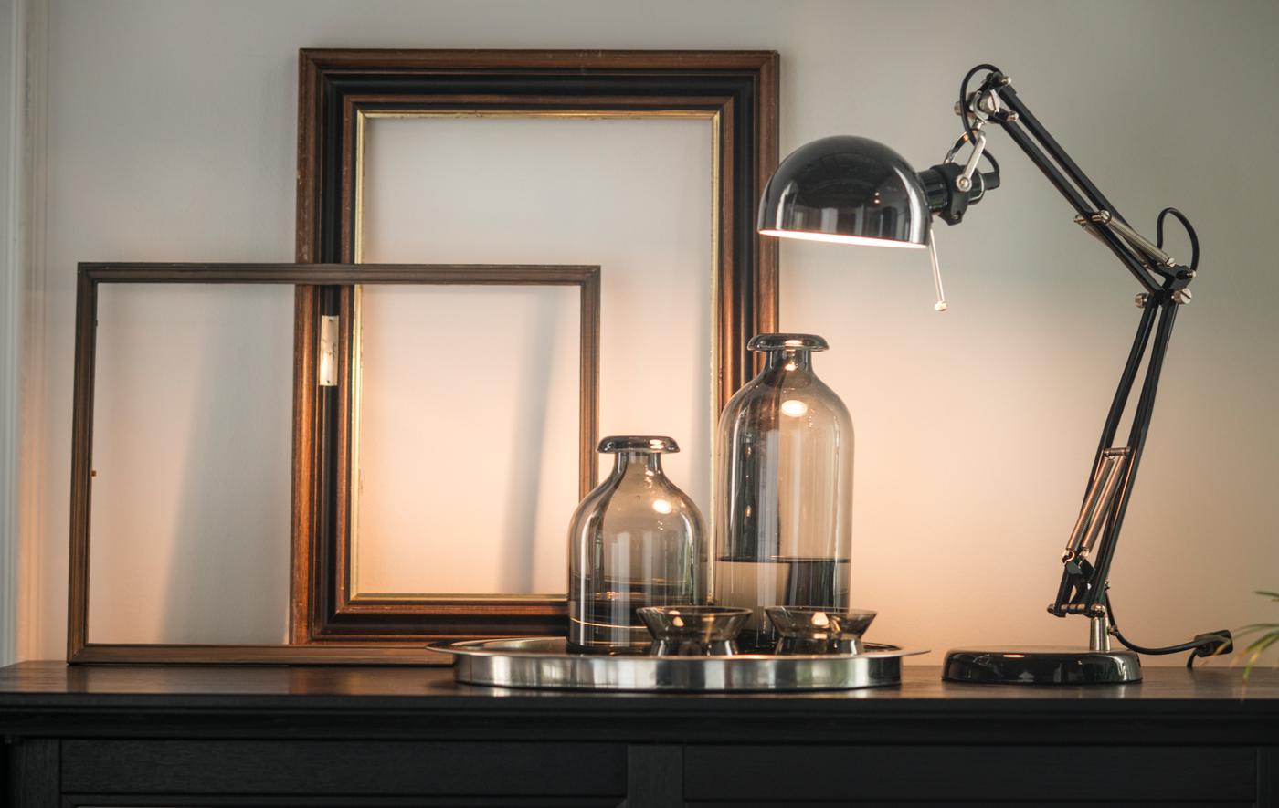 A metallic lamp, glass bottles, and empty frames arranged on top of a black cabinet.