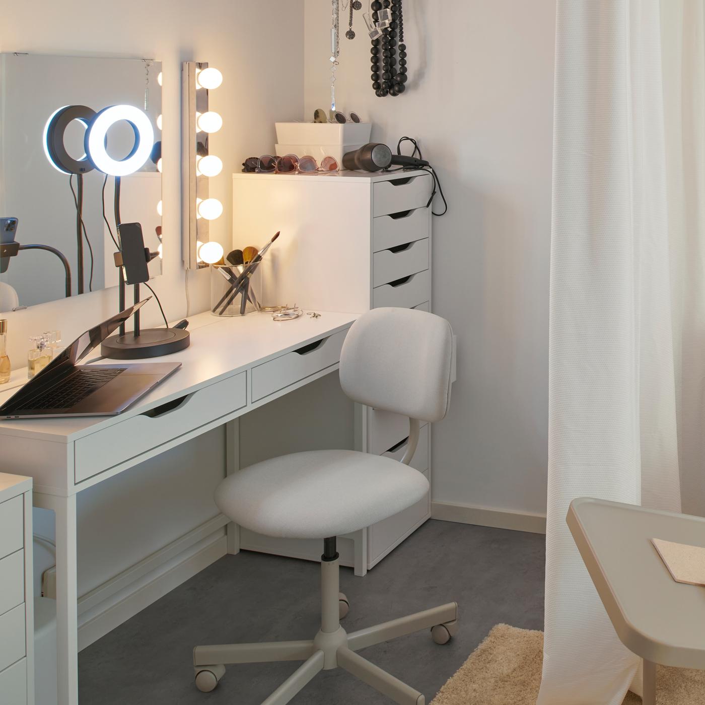 A MICKE desk with a LÅNESPELARE ring light serves as a vanity in a dorm room. A BLECKBERGET swivel chair is at the desk.