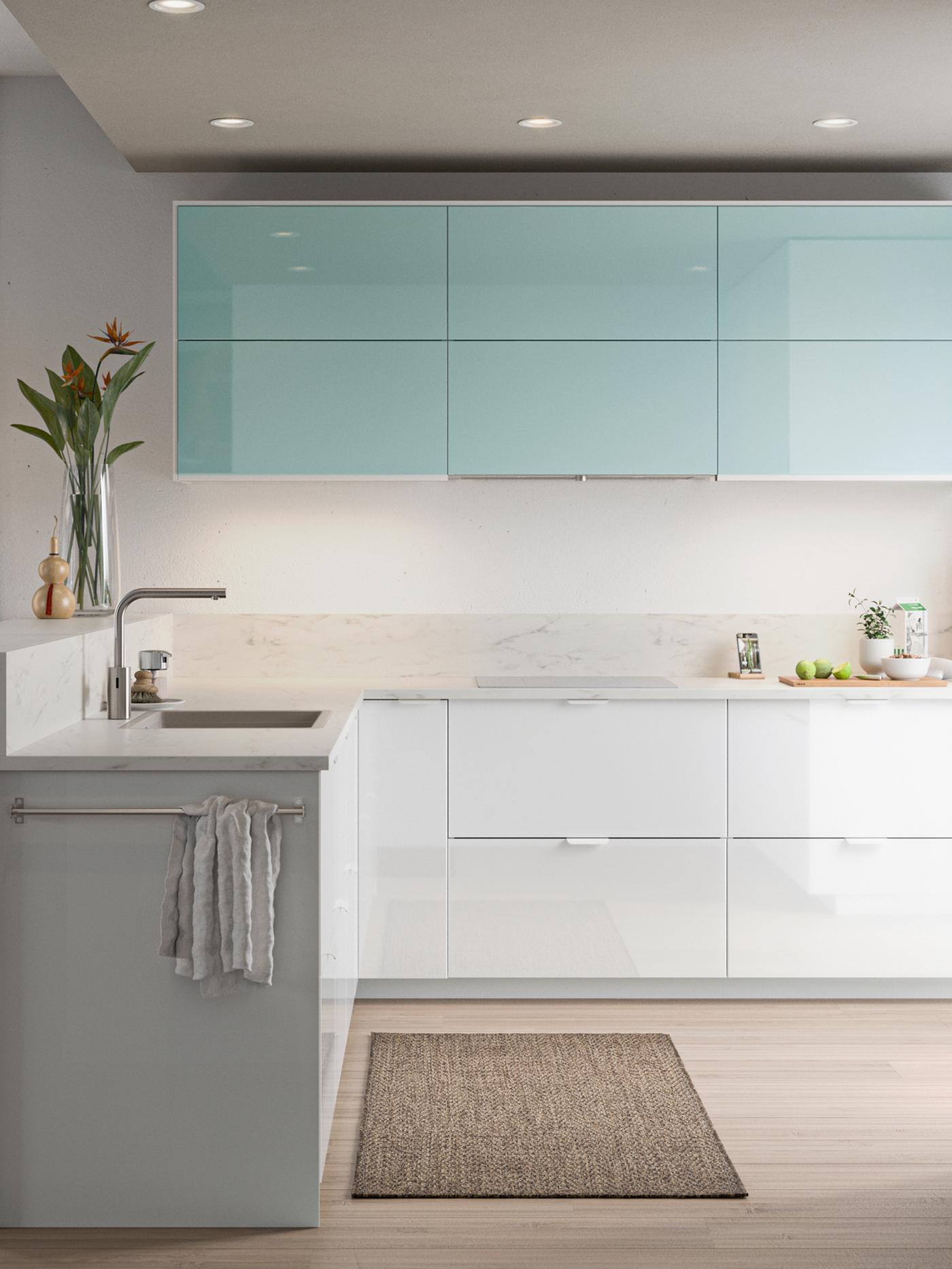 A minimalist kitchen with high-gloss white and light turquoise doors, a sink with a tap and glass vase with flowers.