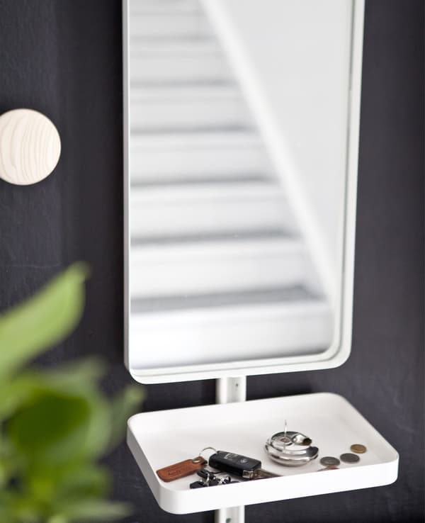 A mirror and small white tray containing keys and coins against a black wall.