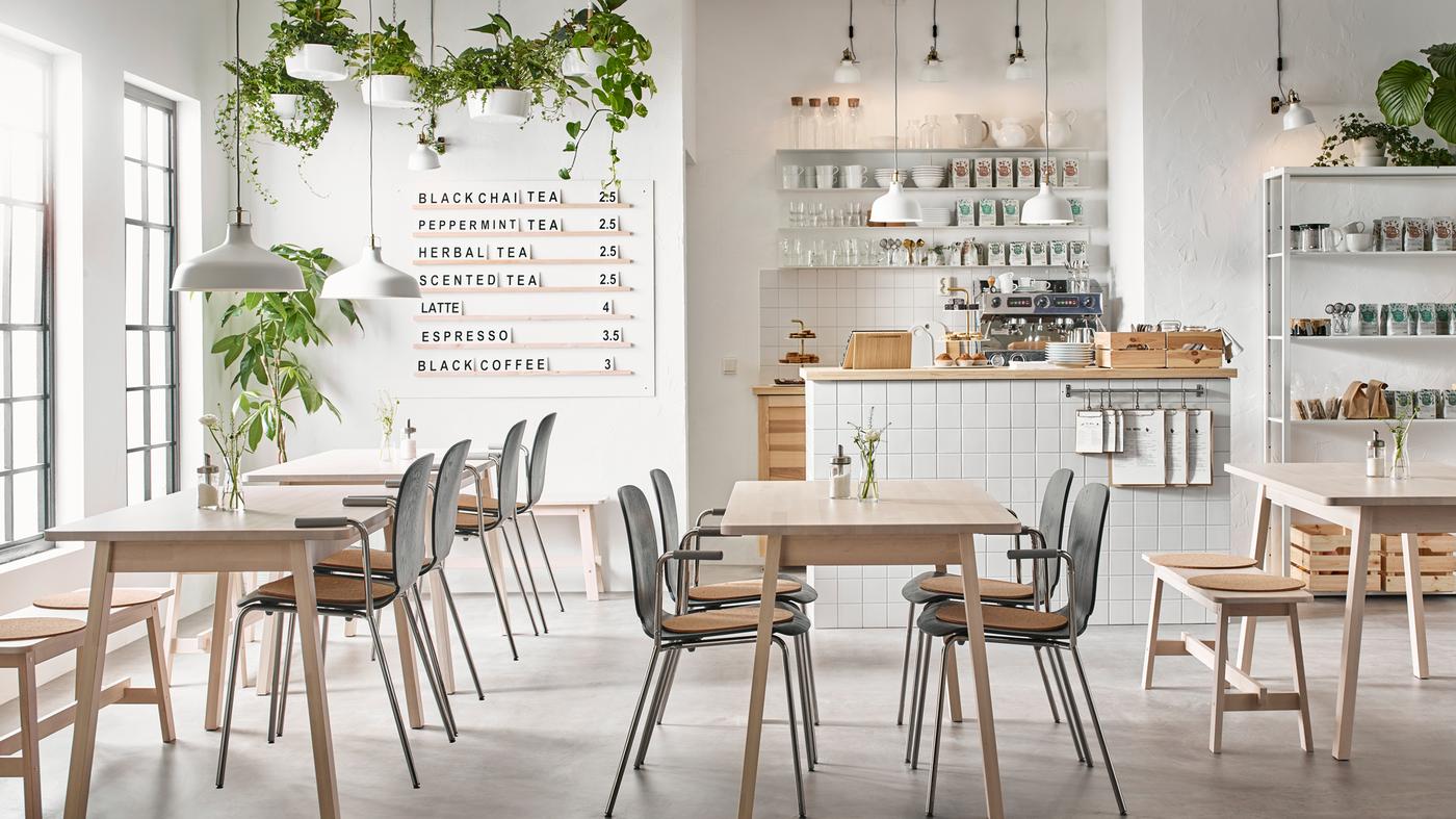 A modern beige, black and white café with white birch NORRÅKER tables and chairs in black and chrome.