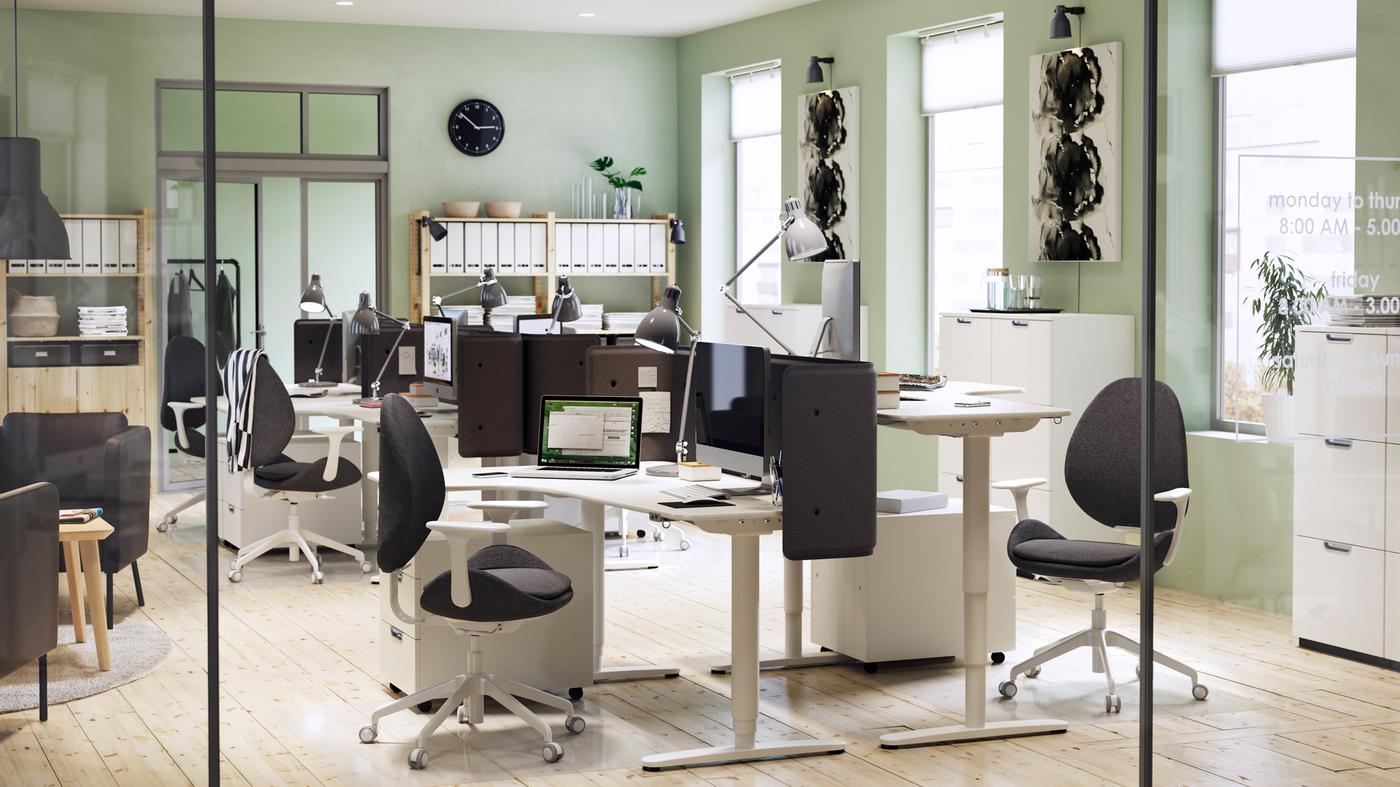 A modern furnished office environment with light green walls and white BEKANT adjustable corner desks and chairs.