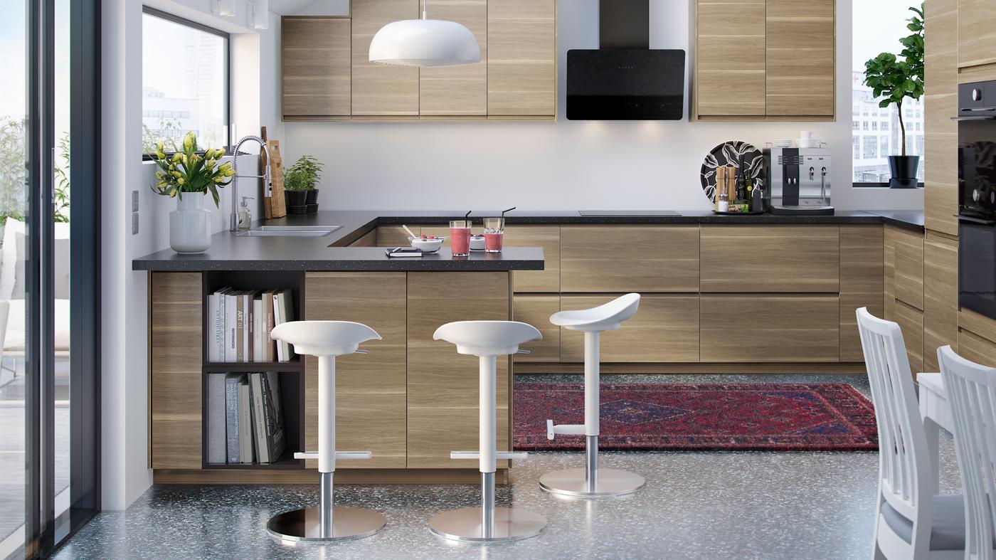A modern kitchen with VOXTORP kitchen fronts in walnut-effect, with three white JANINGE bar stools and NYMÅNE pendant lamp.