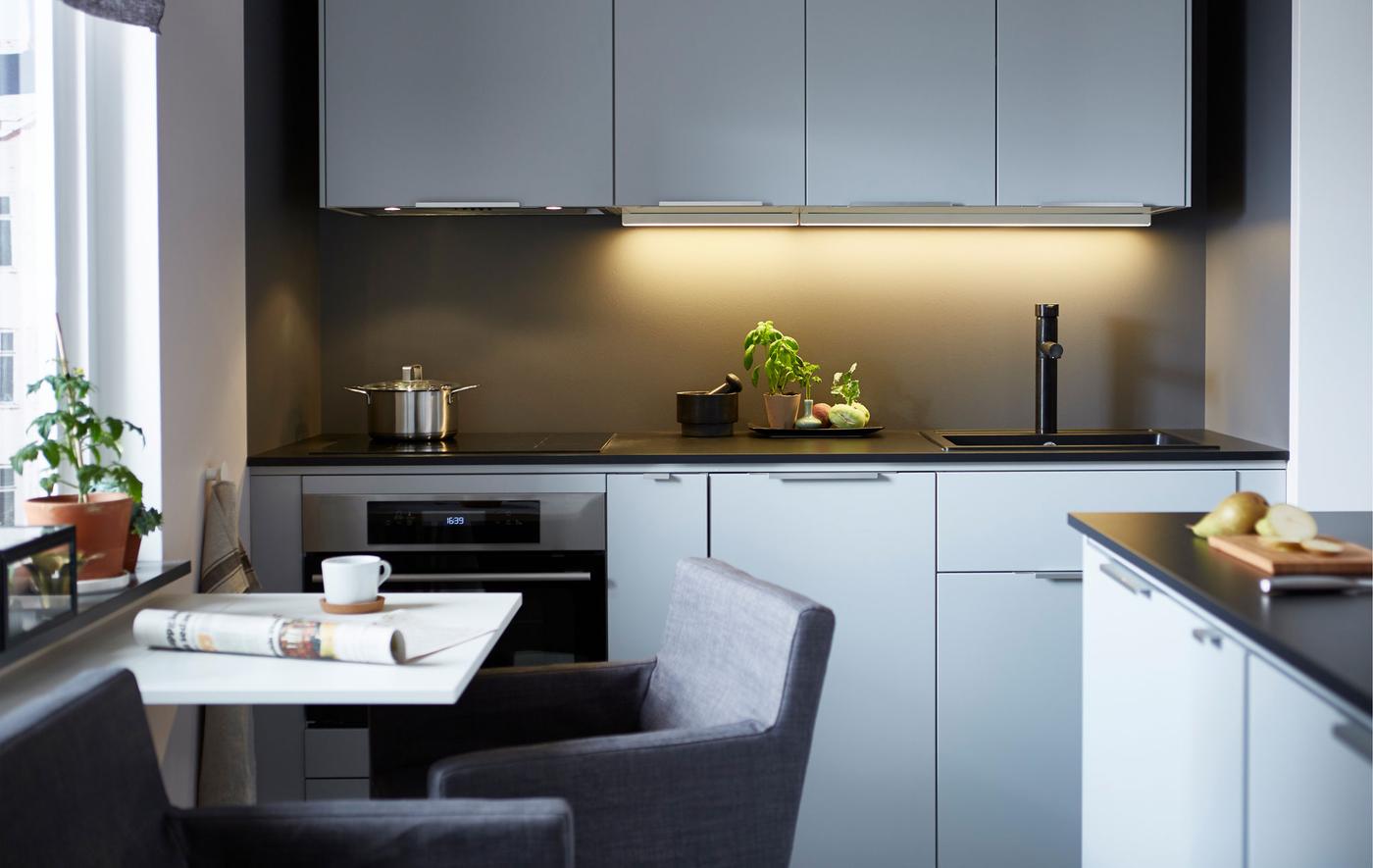 A modern, sleek kitchen with a wall of light-colored cabinets, dark counter tops and a small dining table.