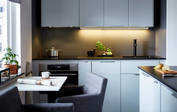 A modern, sleek kitchen with a wall of light-coloured cabinets, dark counter tops and a small dining table
