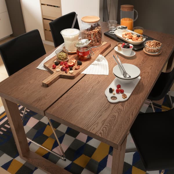 A MÖRBYLÅNGA table made from oak veneer is placed on a carpet. There are a variety of foods and kitchenware on the table.