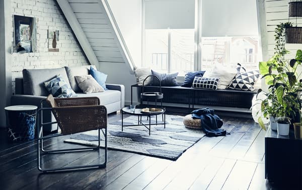 A monochrome living room with a pitched roof, grey sofa, rattan armchair and large textured rug.