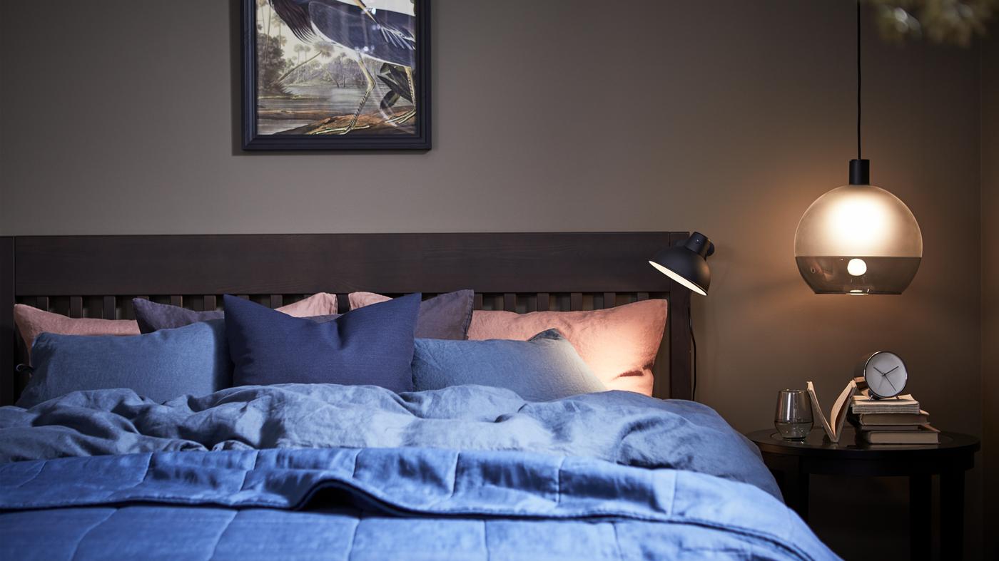 A moodily-lit bedroom with an IDANÄS bed frame with a PUDERVIVA quilt cover and pillowcases in dark blue.