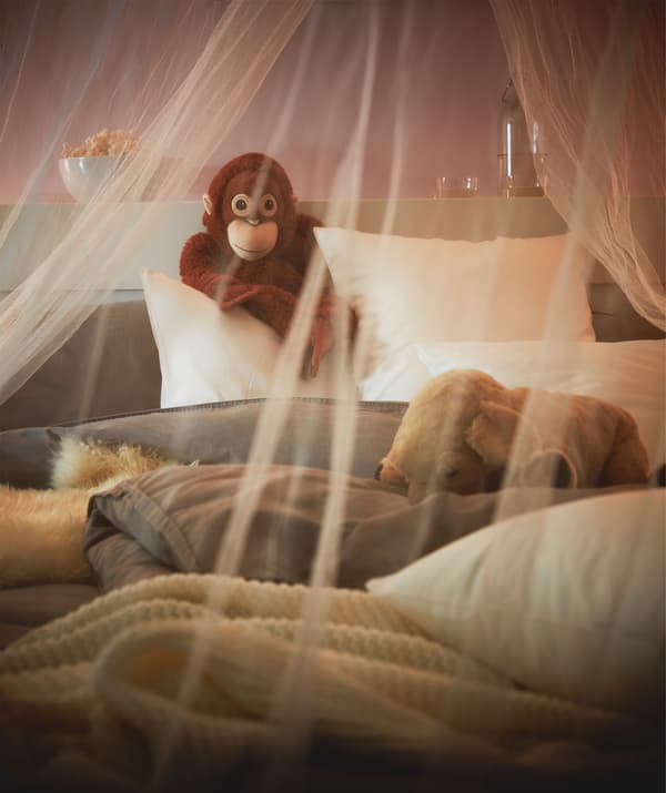 A mosquito net draped over a cozily lit, fluffy, unmade bed, a toy monkey propped up against the headboard.