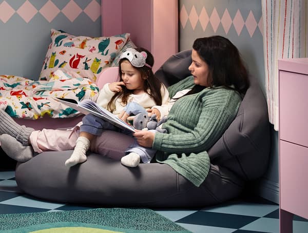 A mother and daughter sitting on a bean bag reading a book.