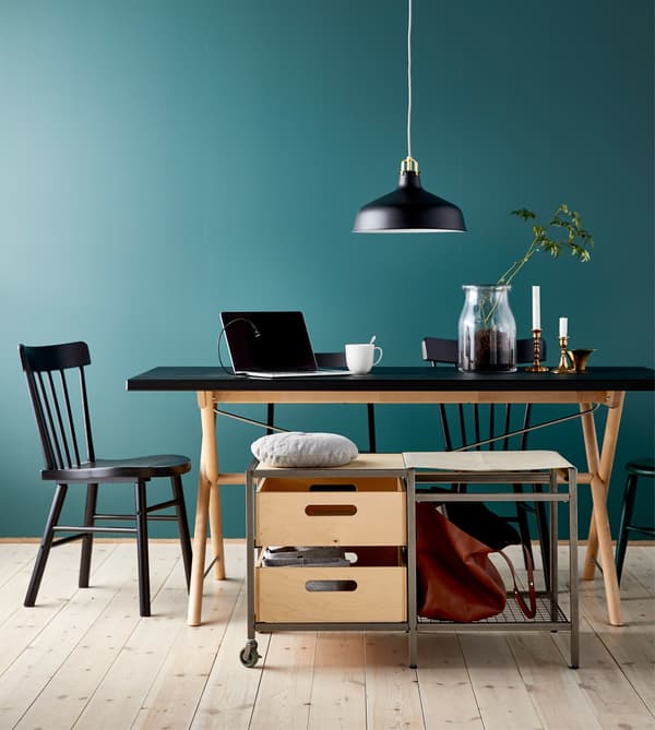 A movable storage bench with castors next to a large dining table that’s being used as a study or work space.