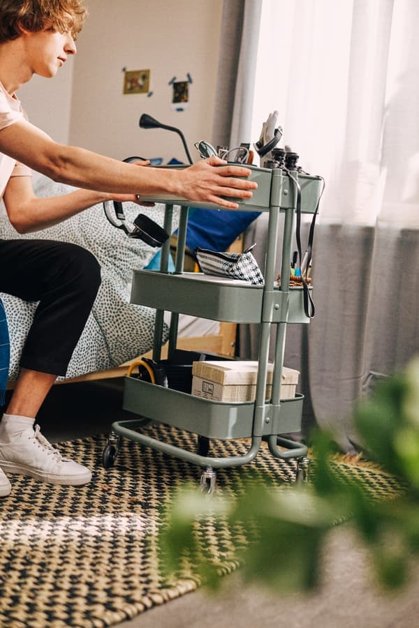 A movable storage with castors next to a bed that’s being used as a study or work space. 