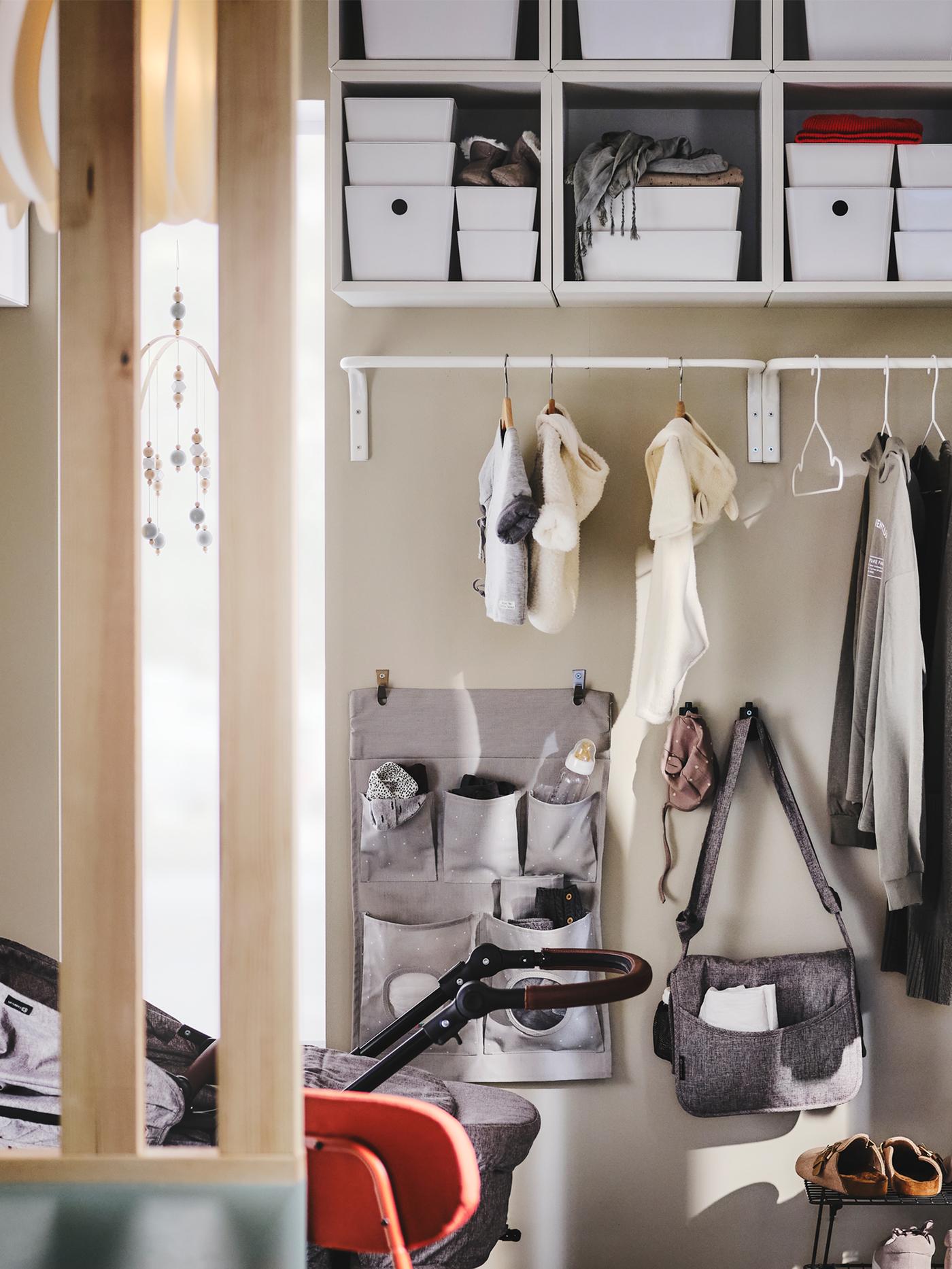 A MULIG clothes bar on a hallway wall holding outdoor clothes, with a LEN hanging storage and hooks on the wall below it.