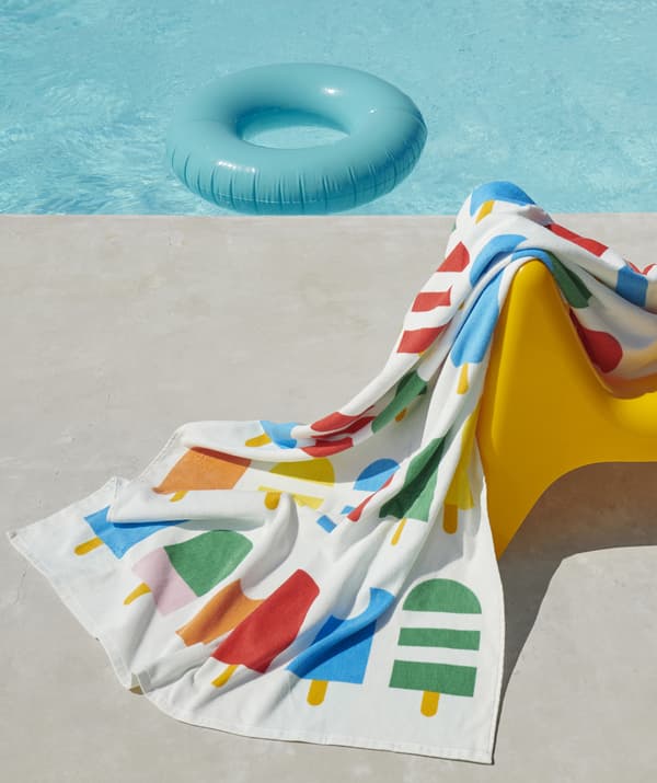 A multicolour towel with ice lolly print on a chair next to a swimming pool in the sunshine.