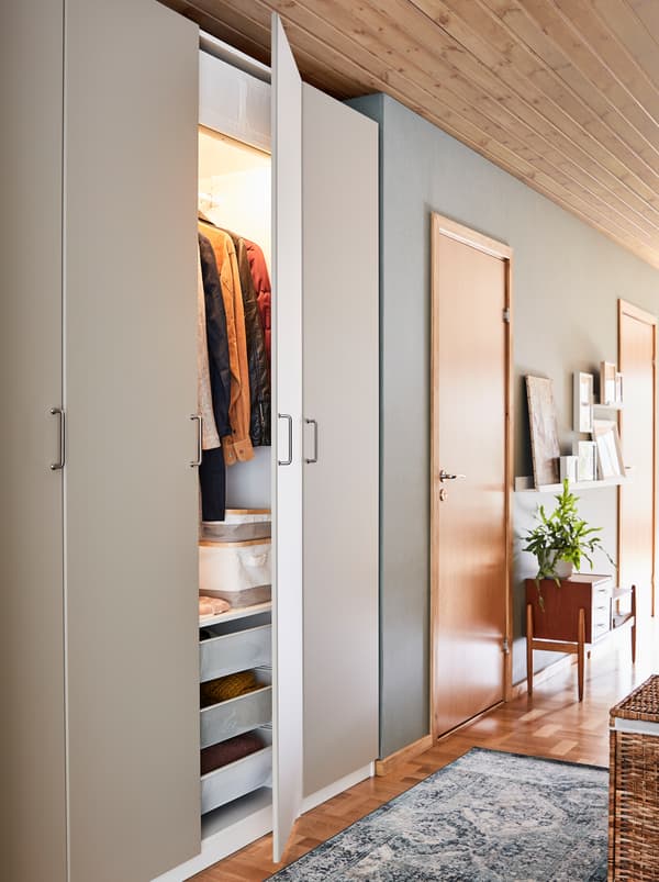 A narrow hallway with a white PAX wardrobe combination with racks, drawers and doors.