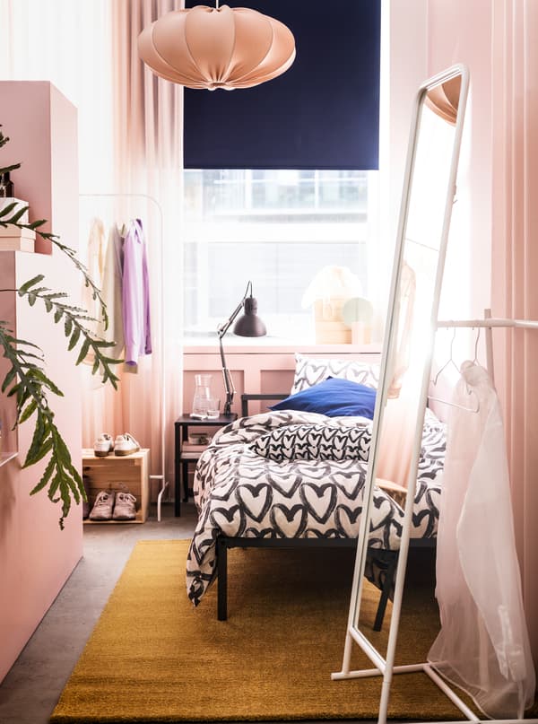 A narrow room in a rosy colour scheme with a GRIMSBU bed, a tall KNAPPER mirror and ample room to store and display clothes.