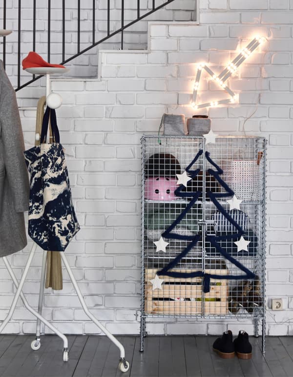 A netted IKEA PS 2017 storage unit cross-stitched with black wool to create a tree on the doorway, with an arrow light.