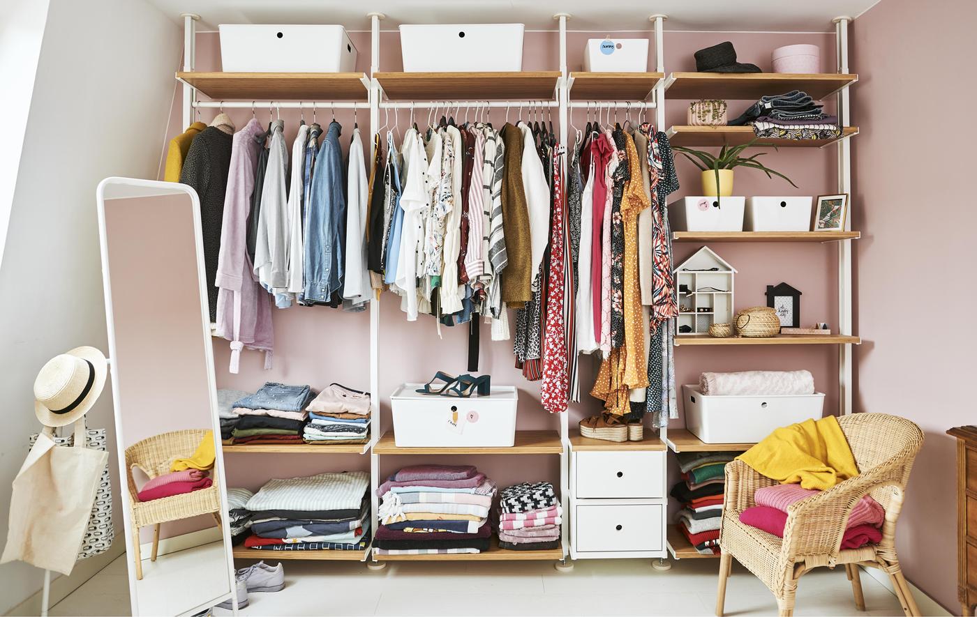 A open wardrobe full of clothes with rails, shelves and boxes set against a pink wall.