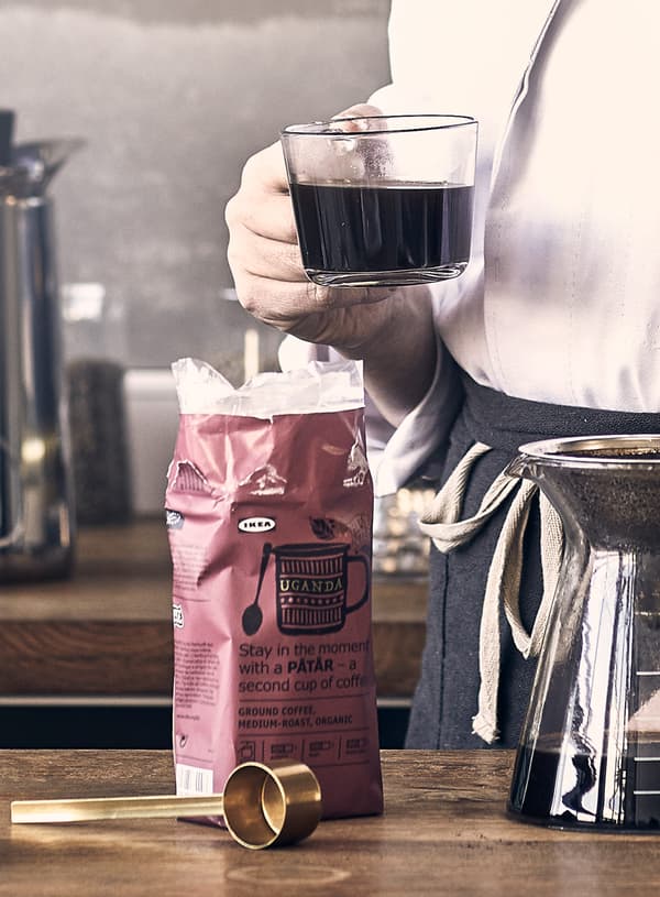 A package of a dark pink IKEA PÅTÅR coffee, brewing equipment and a person holding a cup of coffee.