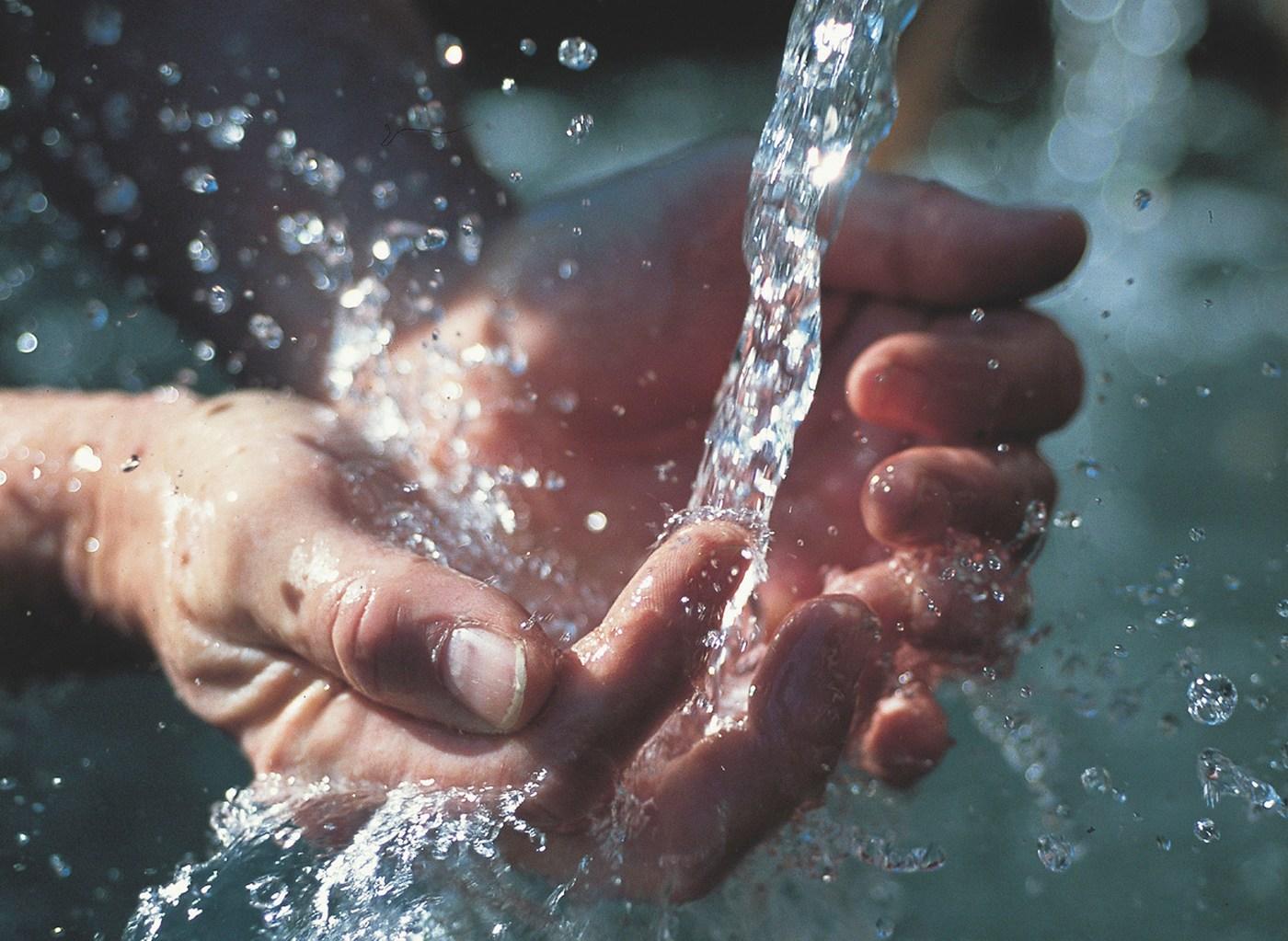 A pair of hands trying to capture water from a running tap.