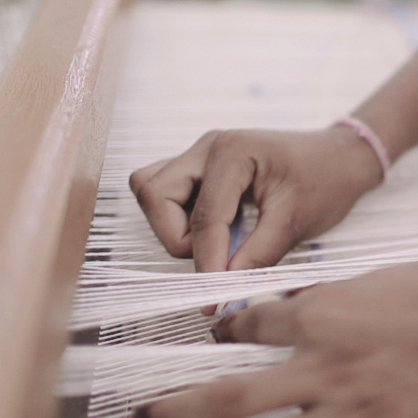 A pair of hands weaving white threads on a loom.