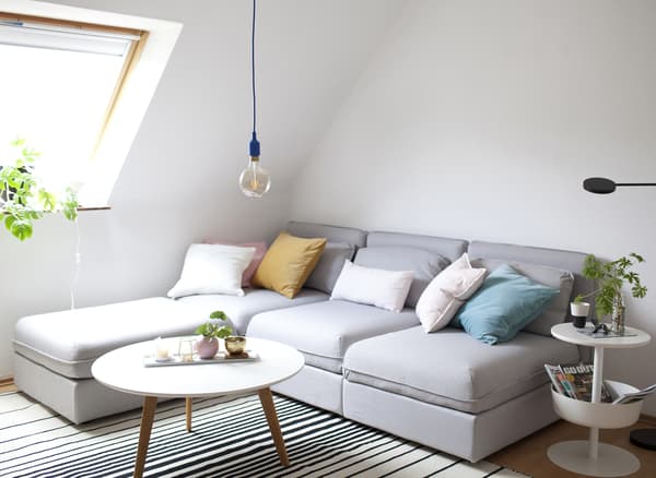 A pale grey corner sofa, striped rug, coffee table and side table with storage.