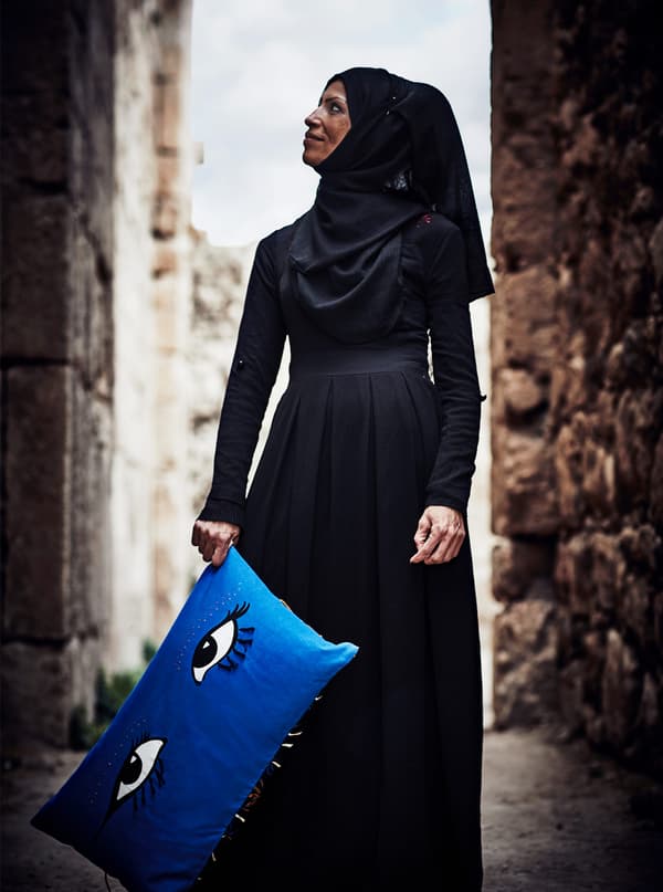 A Palestinian refugee woman artisan is holding a blue cushion with big eyes on it that she made for an IKEA collection.