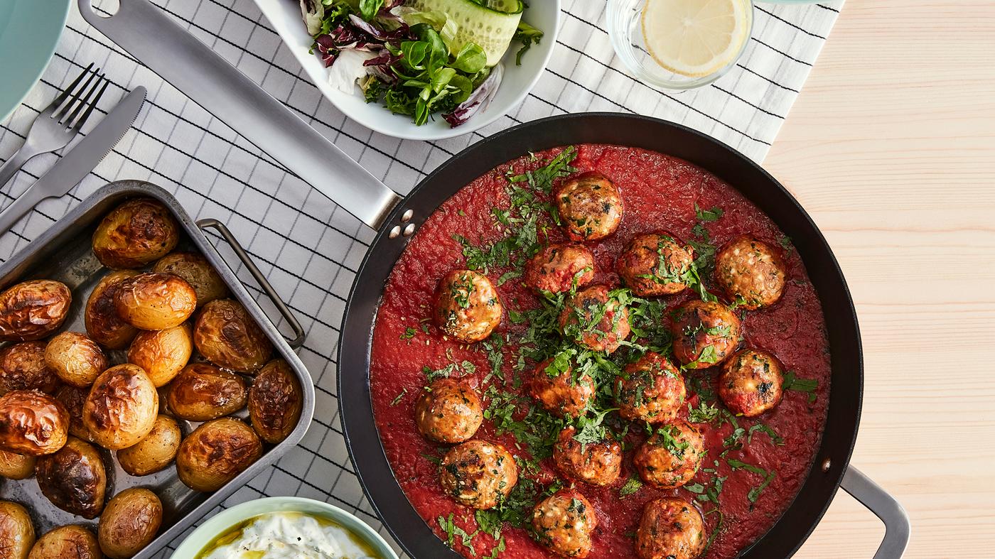 A pan with mince balls, made from VÄRLDSKLOK plant-based mince, in tomato sauce and an oven tray with roasted potatoes.