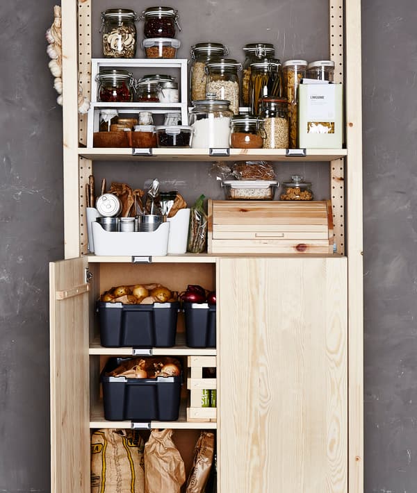 A pantry shelving unit is organized with ingredients in glass and plastic containers. The bottom section has one door open to show vegetable storage.