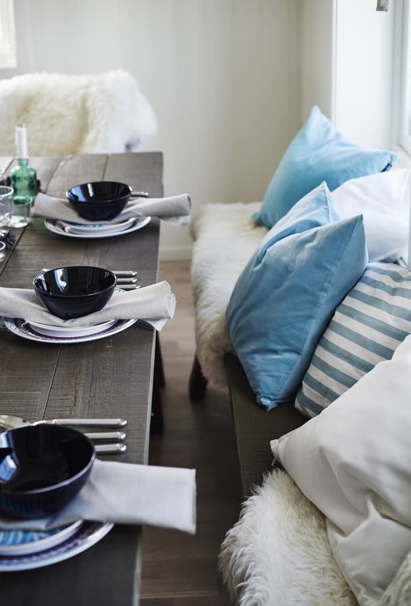 A pastel blue cushion cover on a dining table bench, coupled with a blue and white striped cushion.