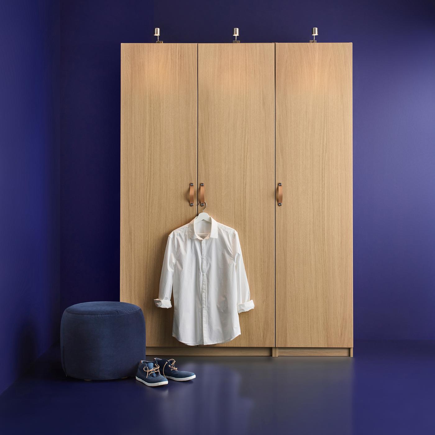 A PAX wardrobe in a blue room with a coat hanger on the door knob holding a white shirt and a pair of shoes on the floor.