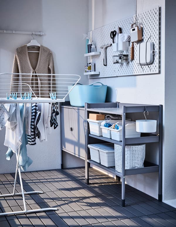 A peg board, storage unit, and wall hooks create a laundry station on a balcony.