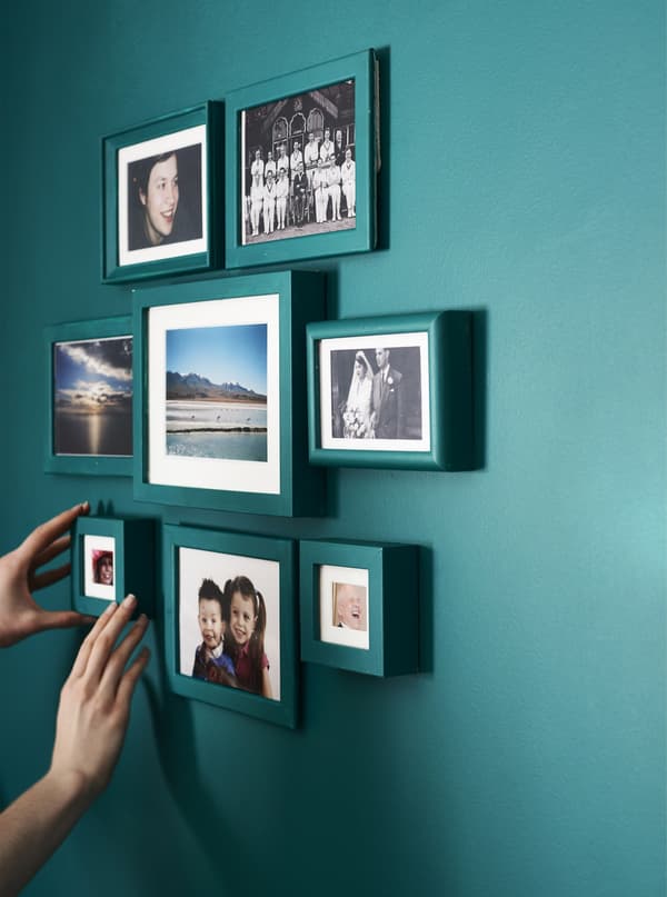 A person adding the final frame to a gallery wall of personal photos.