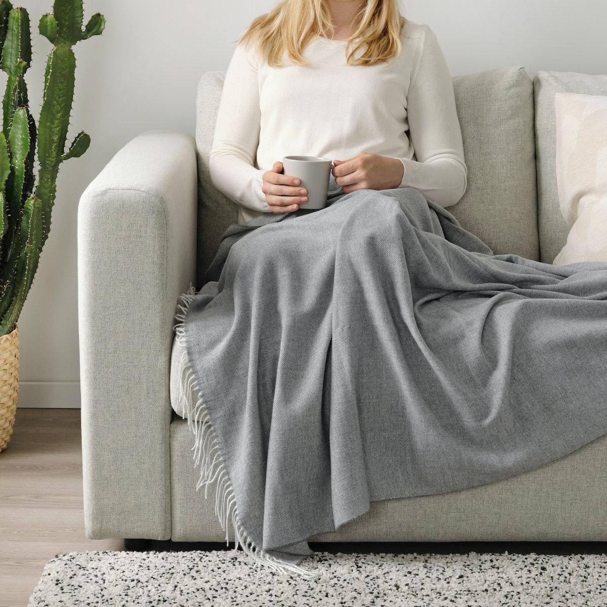 A person comfortably sitting on a couch and holding a cup of hold drink in their hands.