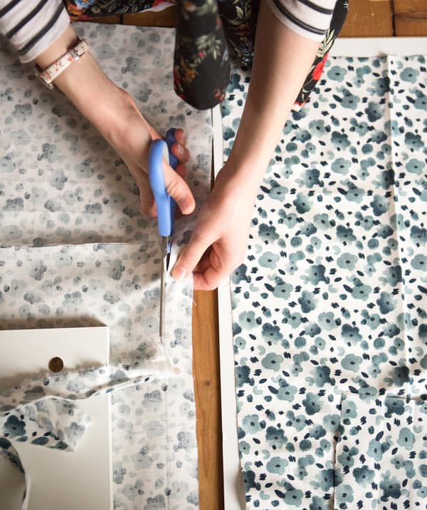 A person cutting through fabric with a blue floral pattern.
