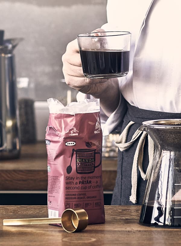 A person holding a cup of coffee made with PÅTÅR special edition coffee and a glass coffee maker for drip coffee.