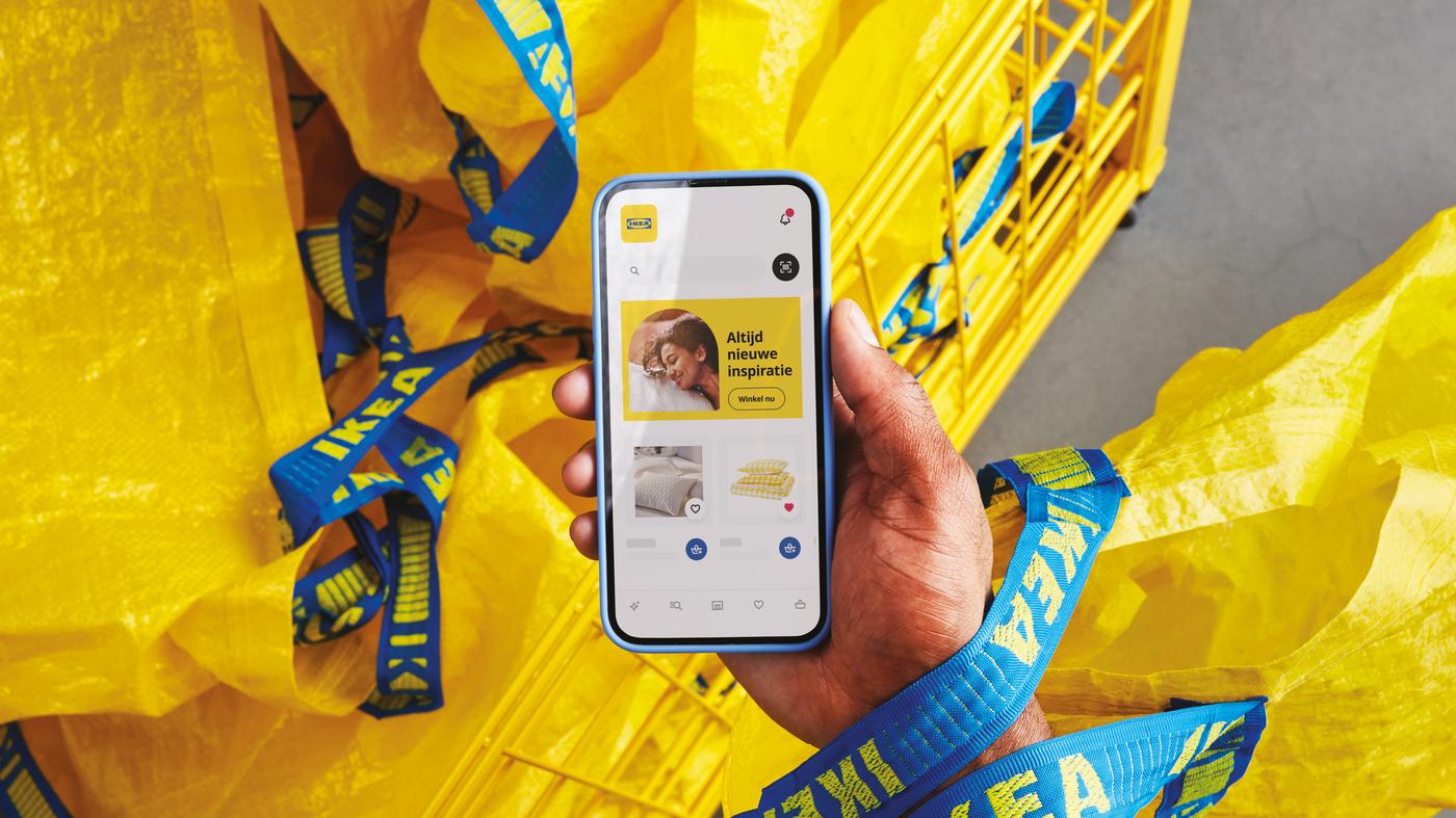 A person holding a yellow IKEA bag and their phone with the IKEA app open