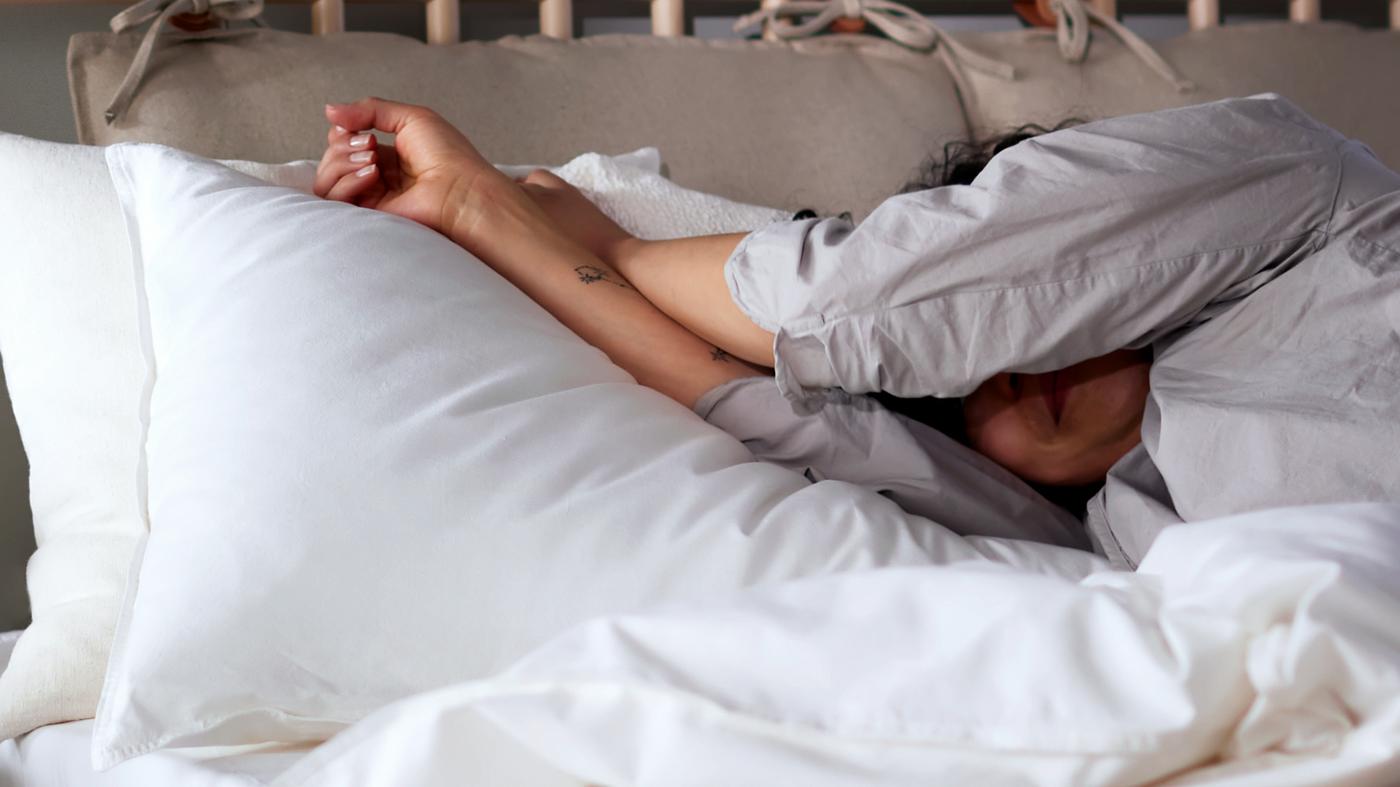 A person in pyjamas lying in a birch BJÖRKSNÄS bed made with white ÄNGSLILJA bed linen.