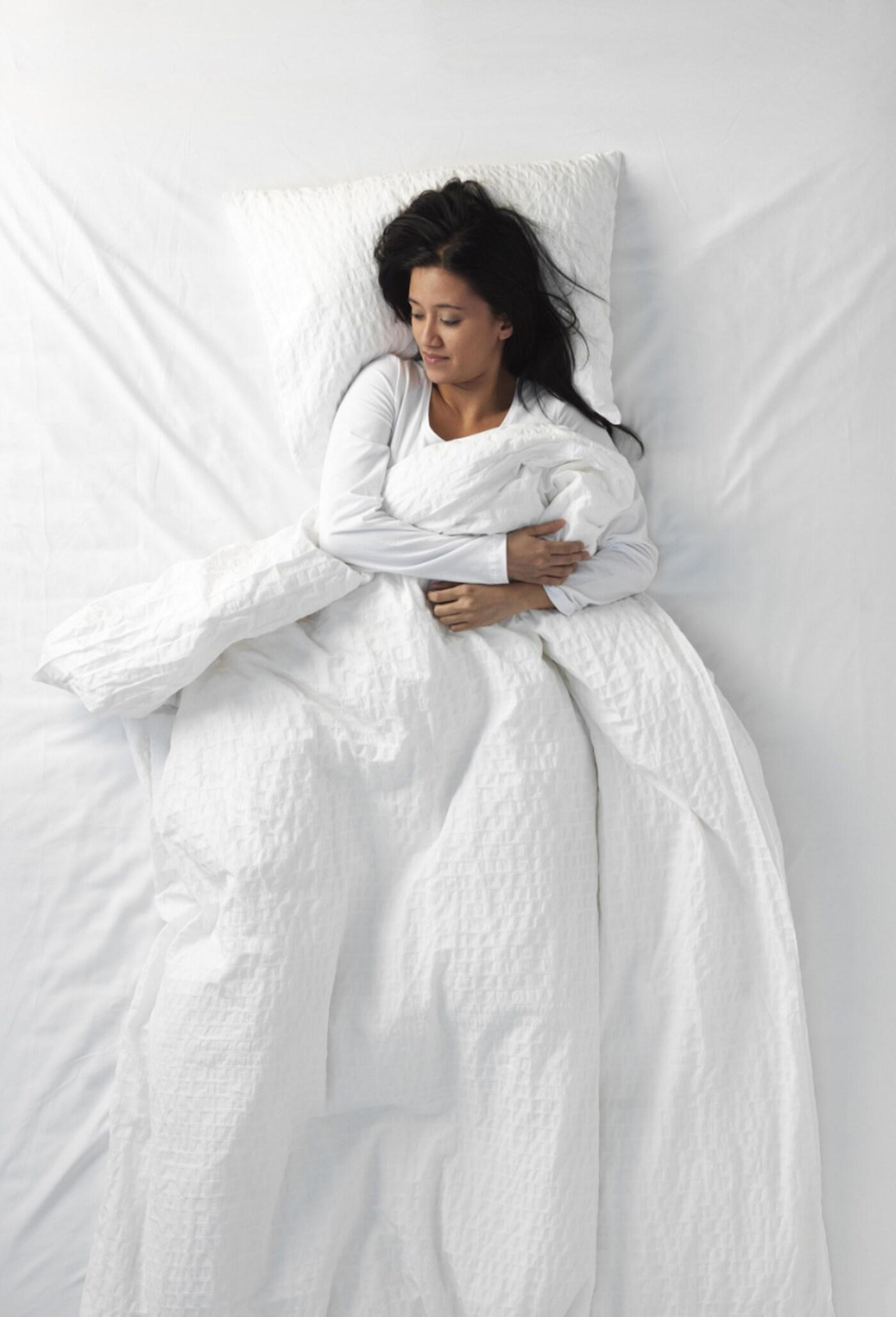 A person lying in her bed on her back.