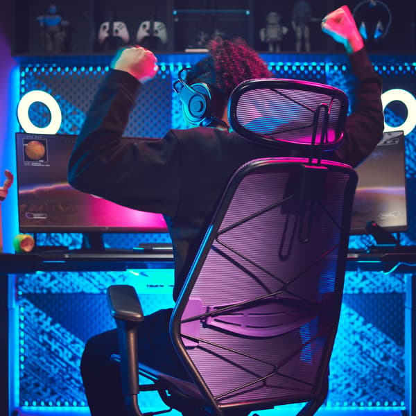 A person playing video games on a gaming desk and chair, the wall lit up with blue neon lights.